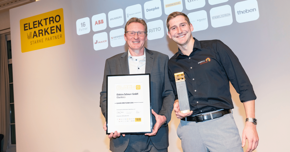 Zwei Vertreter der Elektro Schnurr GmbH stehen auf der Bühne mit ELMAR-Urkunde und -Trophäe. Im Hintergrund sind die Logos der Elektromarken. Starke Partner. zu sehen.