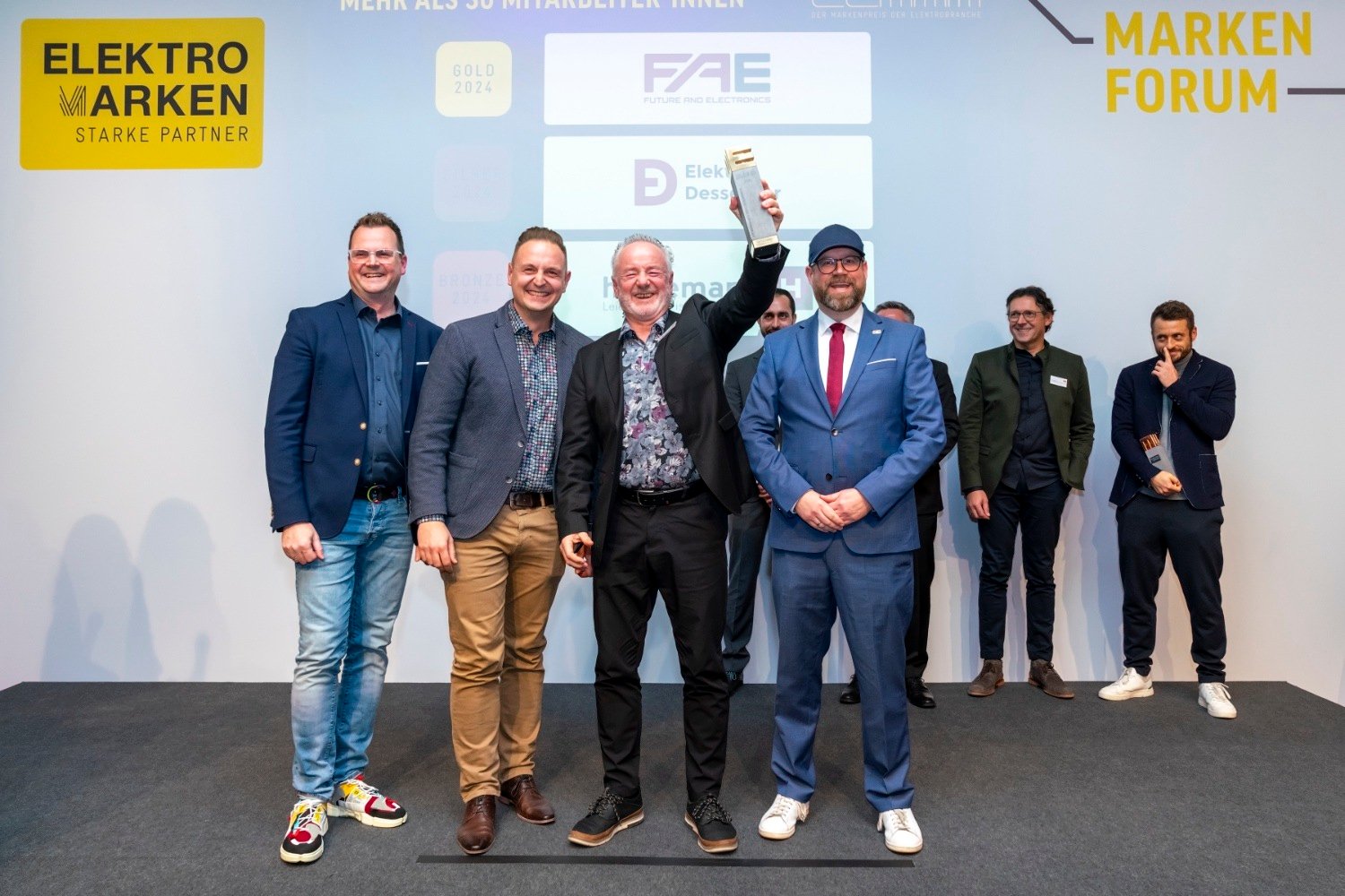 Gewinner des ELMAR 2024 in der Kategorie 'Mehr als 30 MitarbeiterInnen': FAE jubelt auf der Bühne, während die Goldtrophäe stolz präsentiert wird.