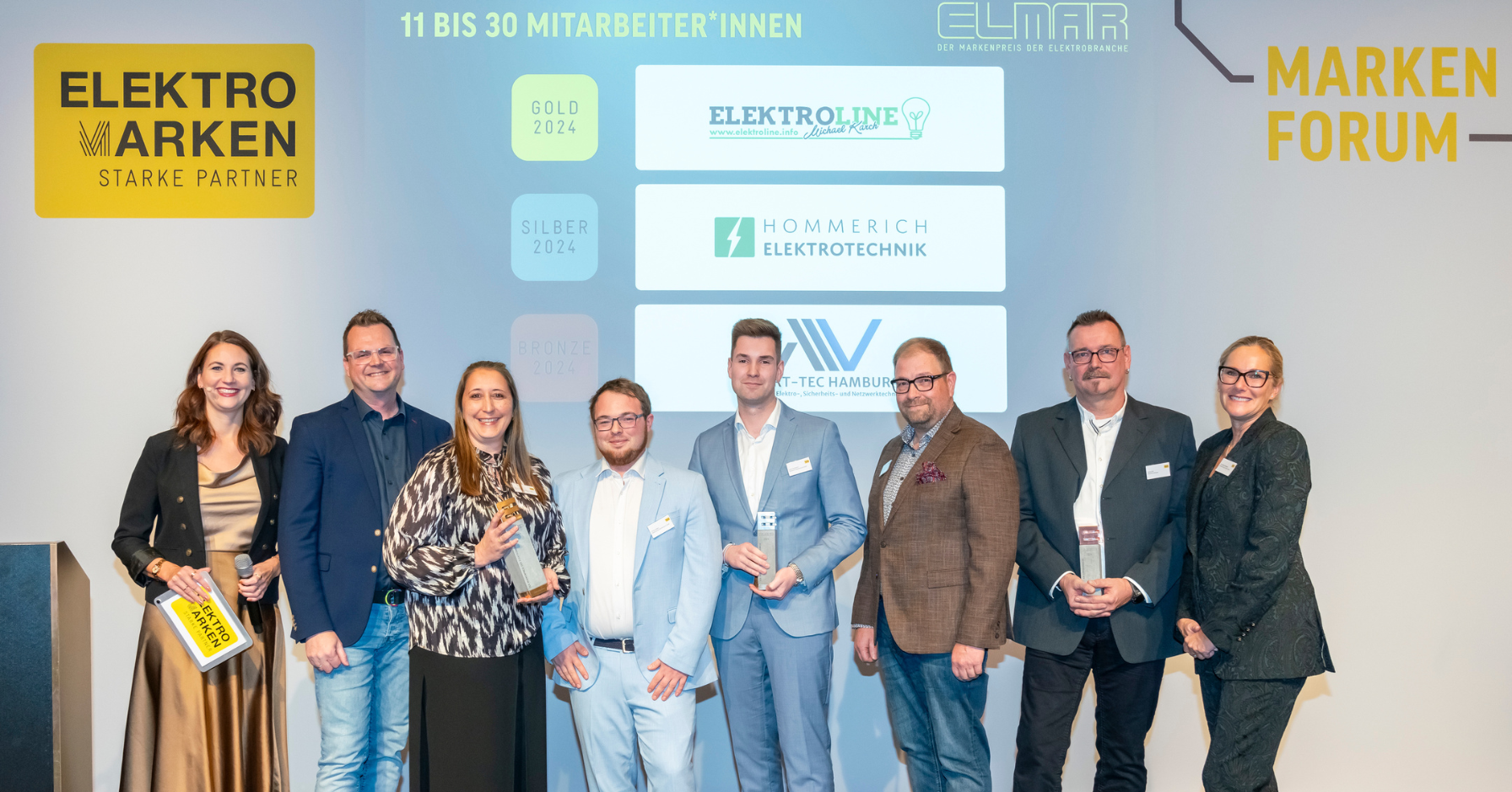 Team von Elektroline by Michael Karch bei der ELMAR-Preisverleihung 2024. Sie halten die Auszeichnung in der Kategorie 11 bis 30 Mitarbeiter auf der Bühne des Markenforums in den Händen.